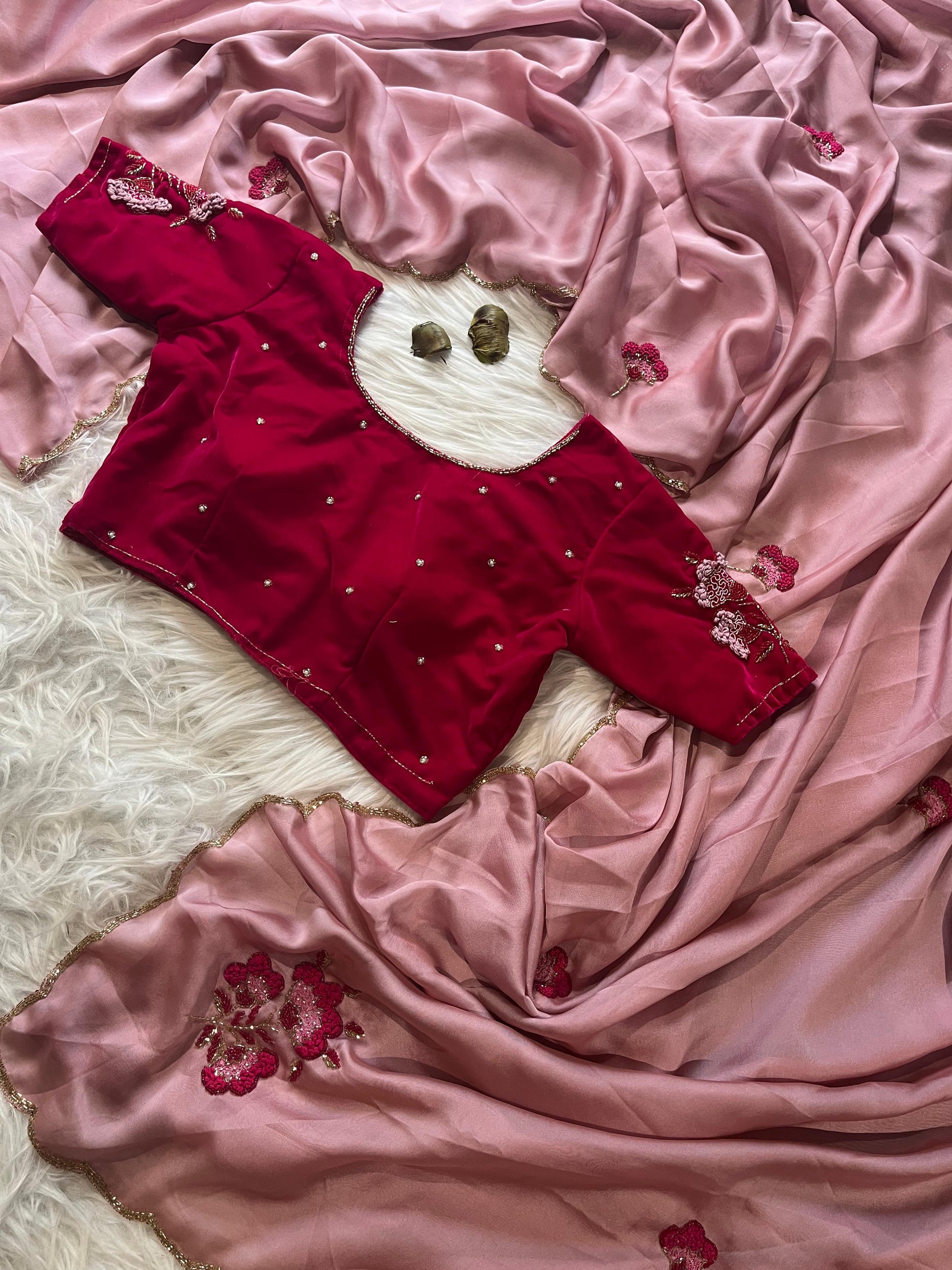 A trendy pink Rangoli silk saree styled with a wine-colored velvet blouse embellished with floral embroidery. The combination of soft silk and rich velvet creates a modern yet traditional festive outfit.