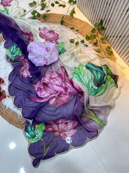 A premium soft organza saree adorned with watercolor-style lotus motifs in vibrant pink and lush green hues. The cream-to-purple gradient and pearl scalloped edging enhance its designer appeal, along with a matching embroidered blouse.