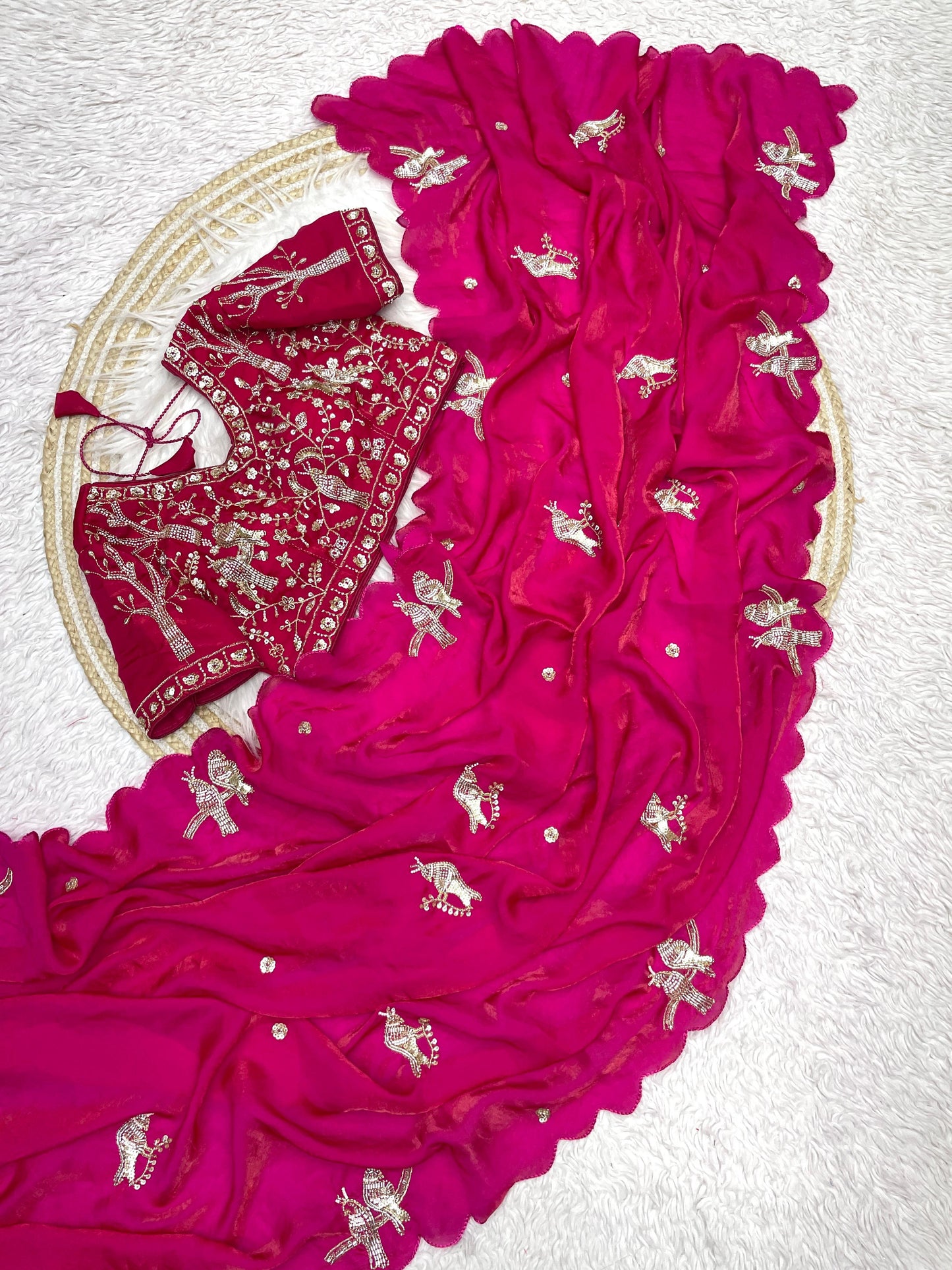 A rich Rani pink silk saree decorated with delicate silver zari bird embroidery and a wavy scalloped border. The ensemble comes with a matching embroidered blouse, giving it a regal and traditional aesthetic.