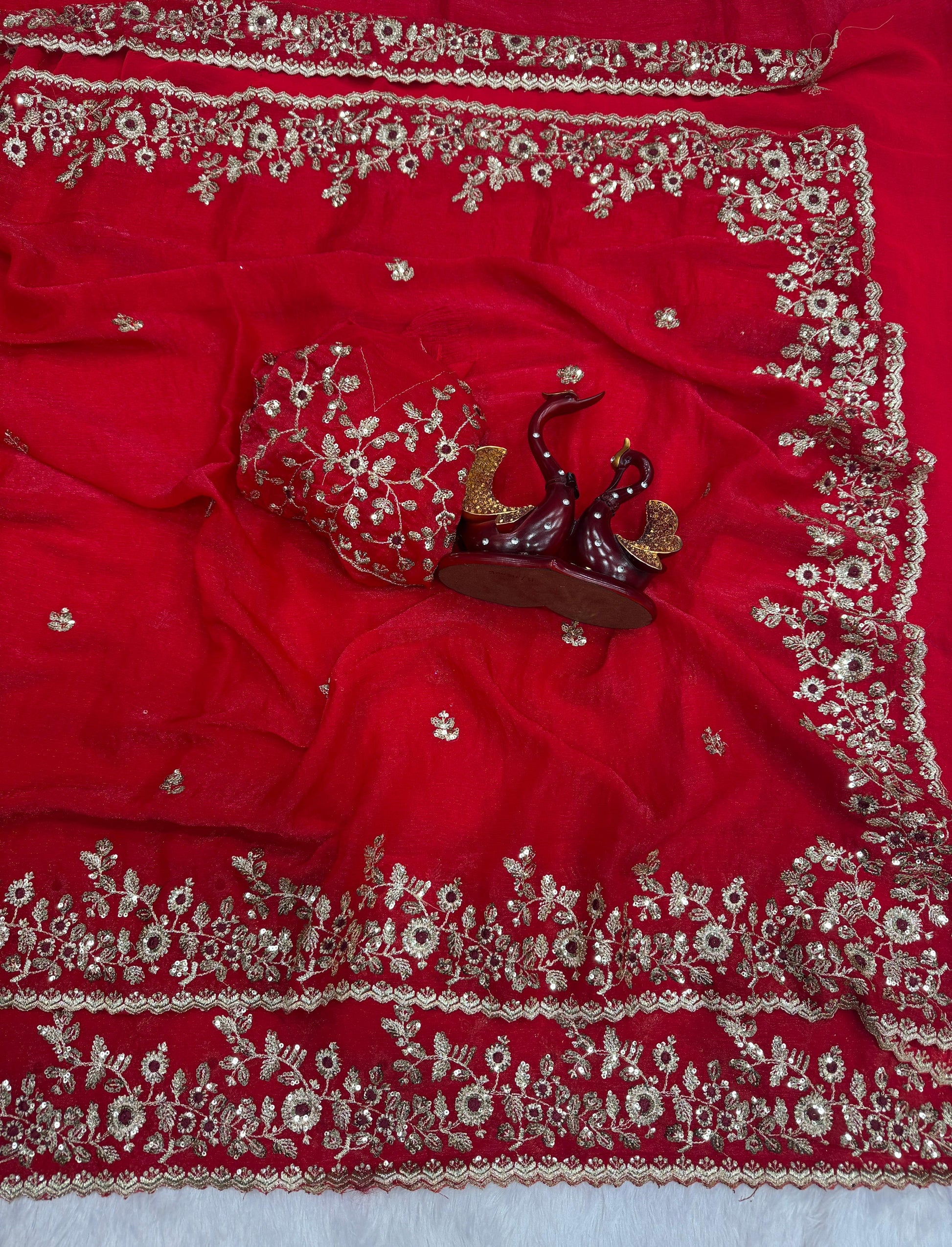 A stunning red Fandy silk saree featuring heavy golden zari embroidery and floral motifs throughout. The matching blouse piece complements the ornate border, making it a luxurious choice for bridal and festive occasions.