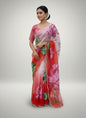 A stunning soft organza saree in shades of red, pink, and white, featuring large hand-painted lotus flowers in vibrant pink and green. The saree is finished with a pearl-embellished scalloped border and includes a matching blouse with lotus artwork, creating an elegant and artistic ethnic look.