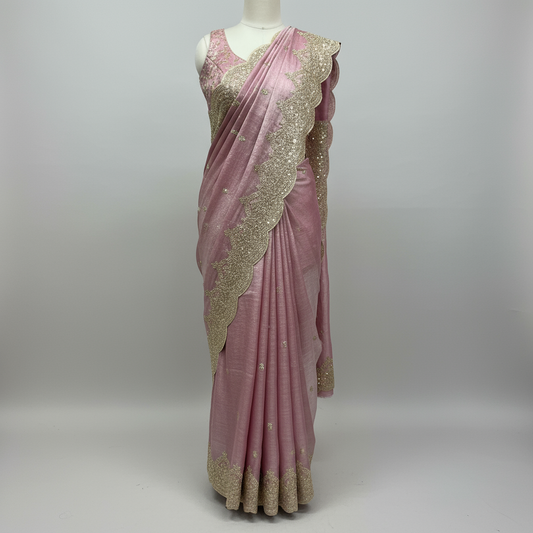 A rose gold saree featuring detailed zari and sequin floral embroidery along a scalloped border. The matching blouse piece adds elegance, making this saree a perfect choice for weddings, receptions, and festive occasions.
