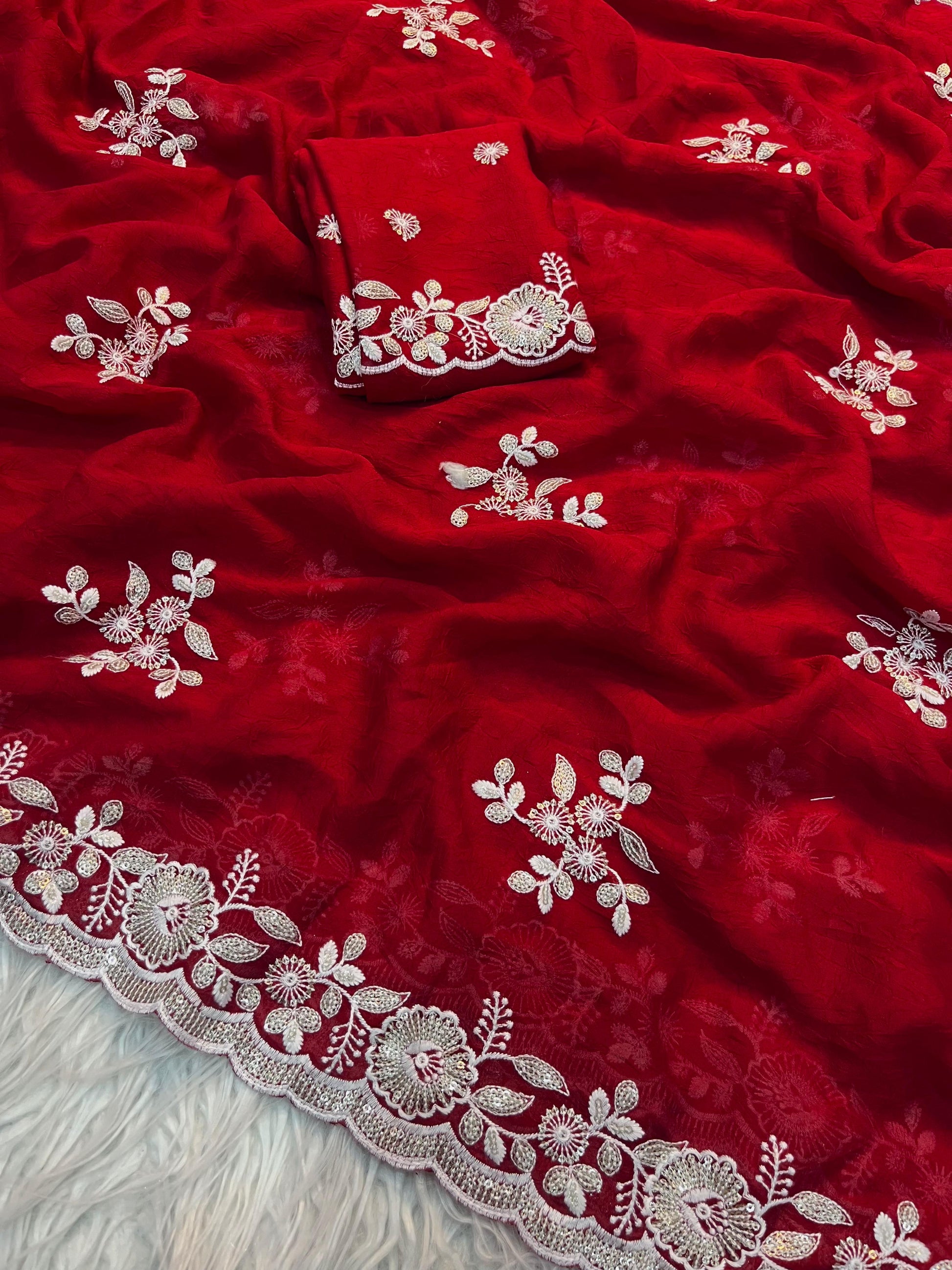 A luxurious scarlet red saree showcasing exquisite zari and thread floral embroidery along the border and throughout the fabric. The matching blouse piece complements the saree’s regal and traditional appeal, perfect for weddings or celebrations.
