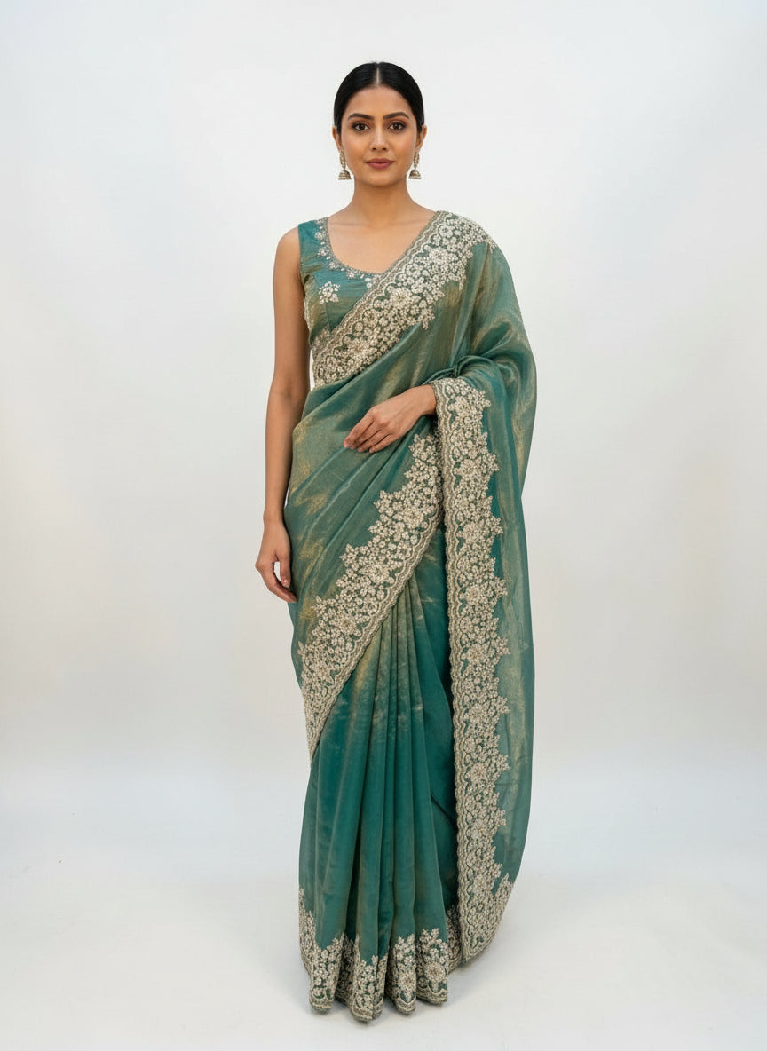 A soft sky blue Fandy silk saree adorned with intricate white floral embroidery along the border. The saree is paired with a matching embroidered blouse featuring coordinating floral motifs, creating an elegant and festive ethnic ensemble.