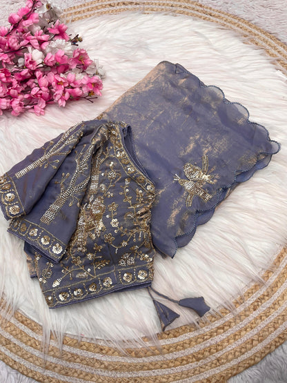 A smoky grey space silk saree highlighted with golden handcrafted bird embroidery and small sequin embellishments. The outfit includes a matching embroidered blouse, making it perfect for weddings and festive occasions.