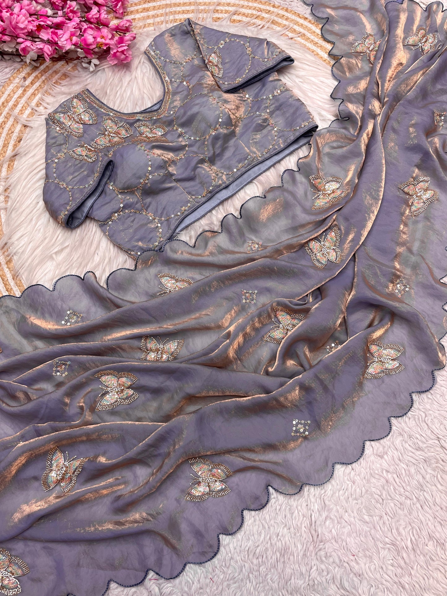 A smoky grey space silk saree decorated with delicate butterfly sequin motifs and wavy scalloped borders. The ensemble includes a matching stitched blouse with complementing embroidery, giving it a modern and elegant charm.