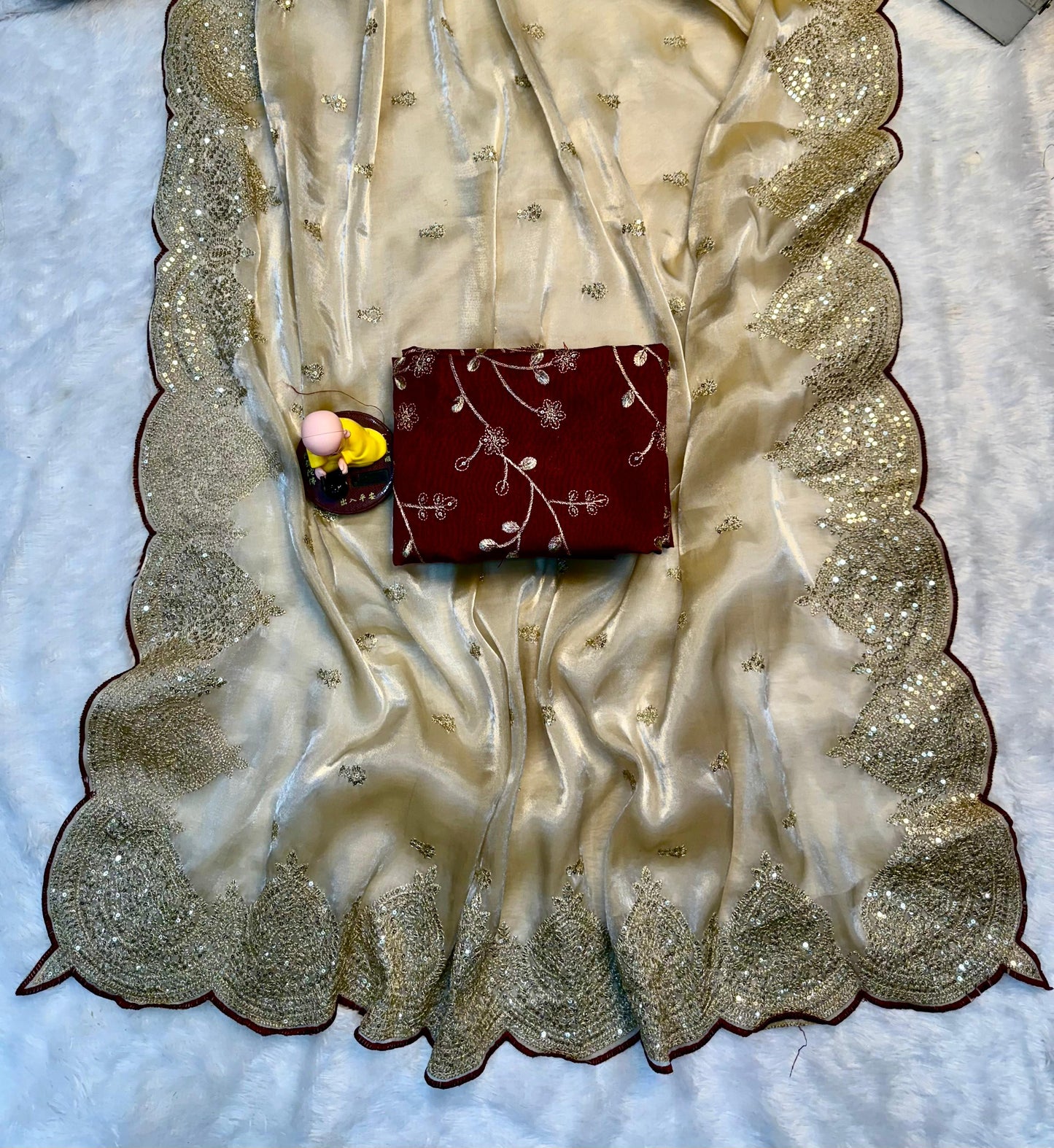 A soft beige saree with glittering floral embroidery and a broad scalloped golden lace border. The saree is complemented by a deep maroon blouse, giving it a stylish and contemporary ethnic appeal.