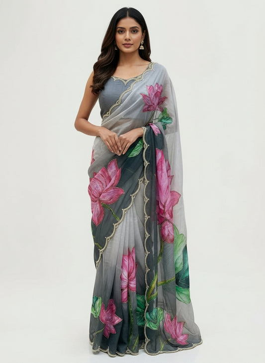 A soft organza saree featuring stunning hand-painted lotus designs in vibrant pink and green shades. The saree has a pearl-embellished scalloped border and comes with a matching blouse showcasing lotus motifs, creating a graceful and artistic ethnic look.