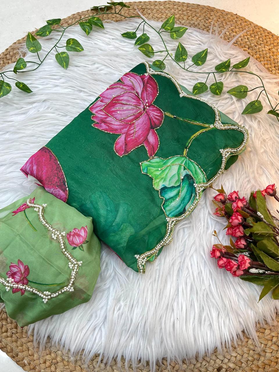 A soft organza saree showcasing vibrant lotus prints in shades of pink and green, finished with a pearl-detailed scalloped border. The matching blouse features lotus embroidery, completing the elegant ensemble.