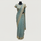 A luxurious teal blue organza saree beautifully adorned with intricate golden embroidery and heavy sequin work along the scalloped border. The saree is paired with a matching embroidered blouse piece and displayed with elegant accessories, exuding a regal and festive charm.